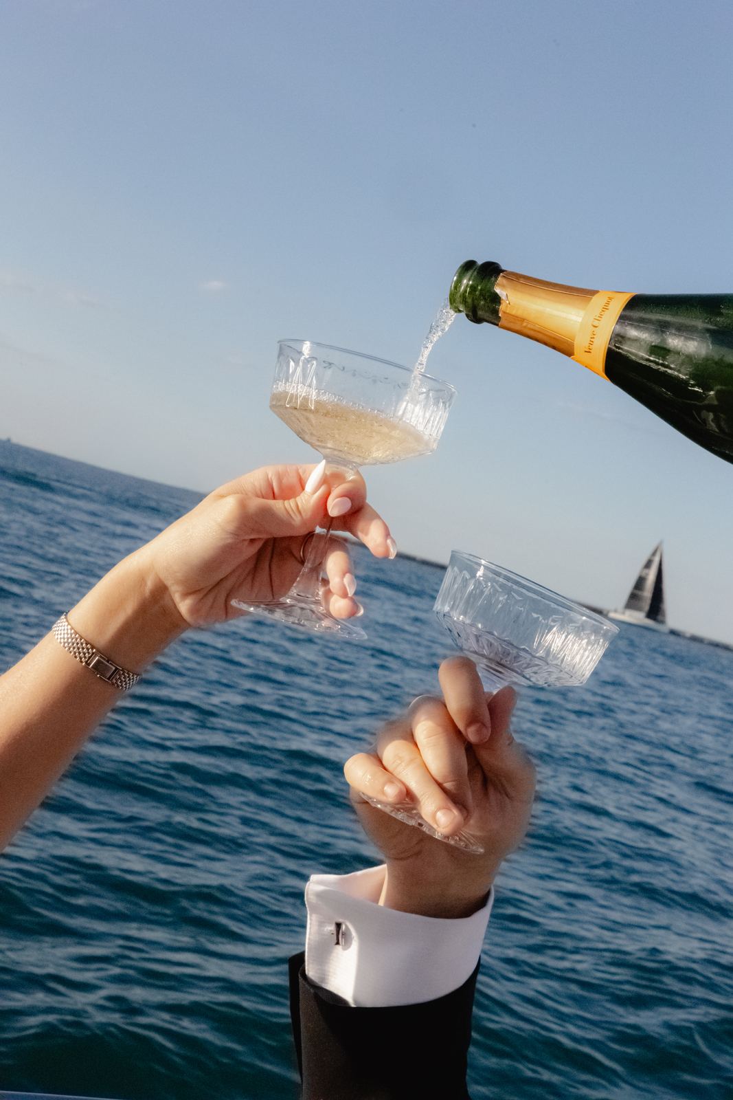 Champagne poured into crystal coupes over open water with a sailboat