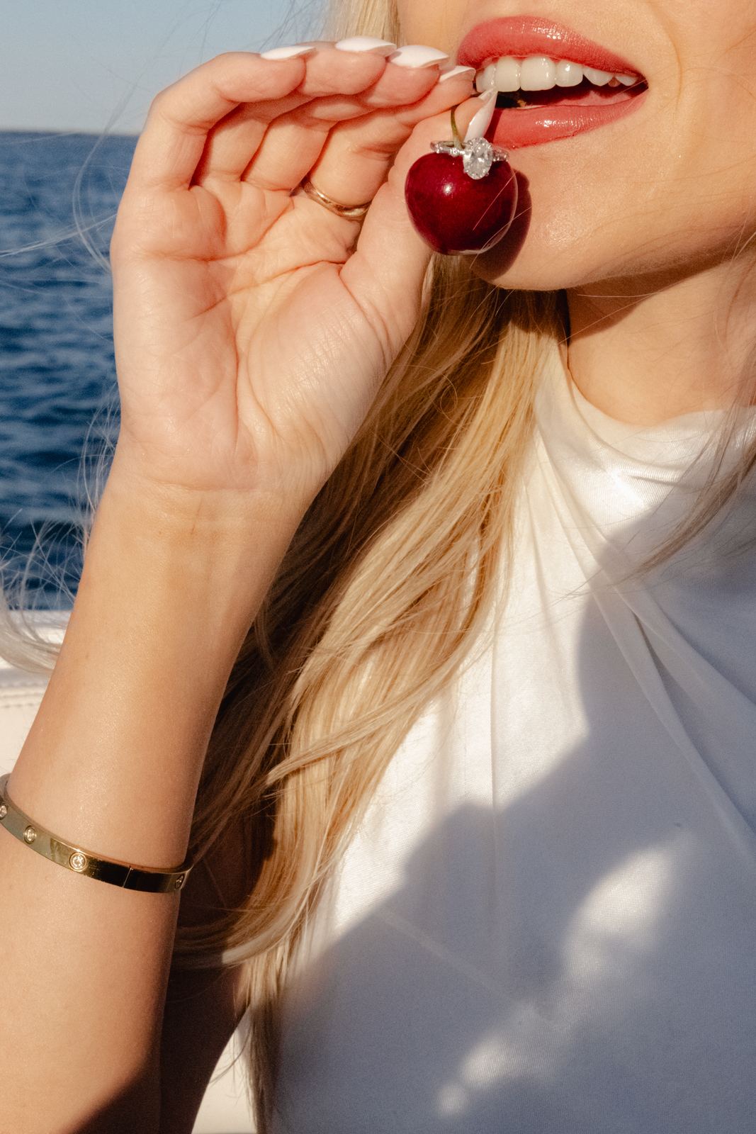 Woman biting a cherry, a gold bangle on her wrist