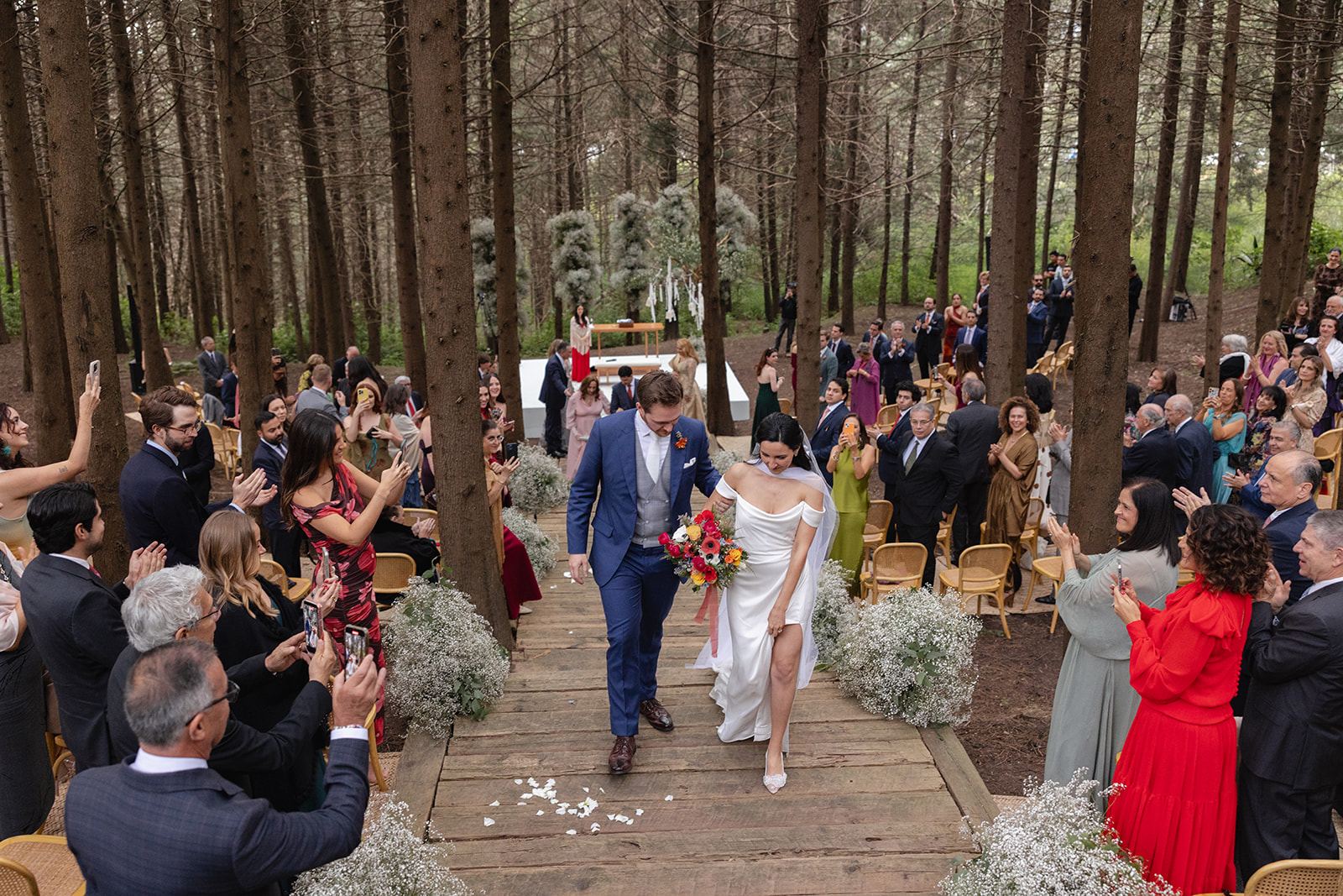 Guests cheering as newlyweds exit a ceremony in a pine forest