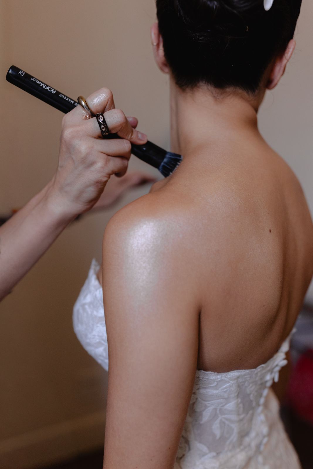 Makeup artist applying shimmer to the bride's bare shoulder