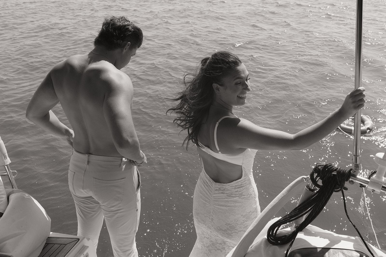 Shirtless man and woman in a white dress laughing at the boat's edge