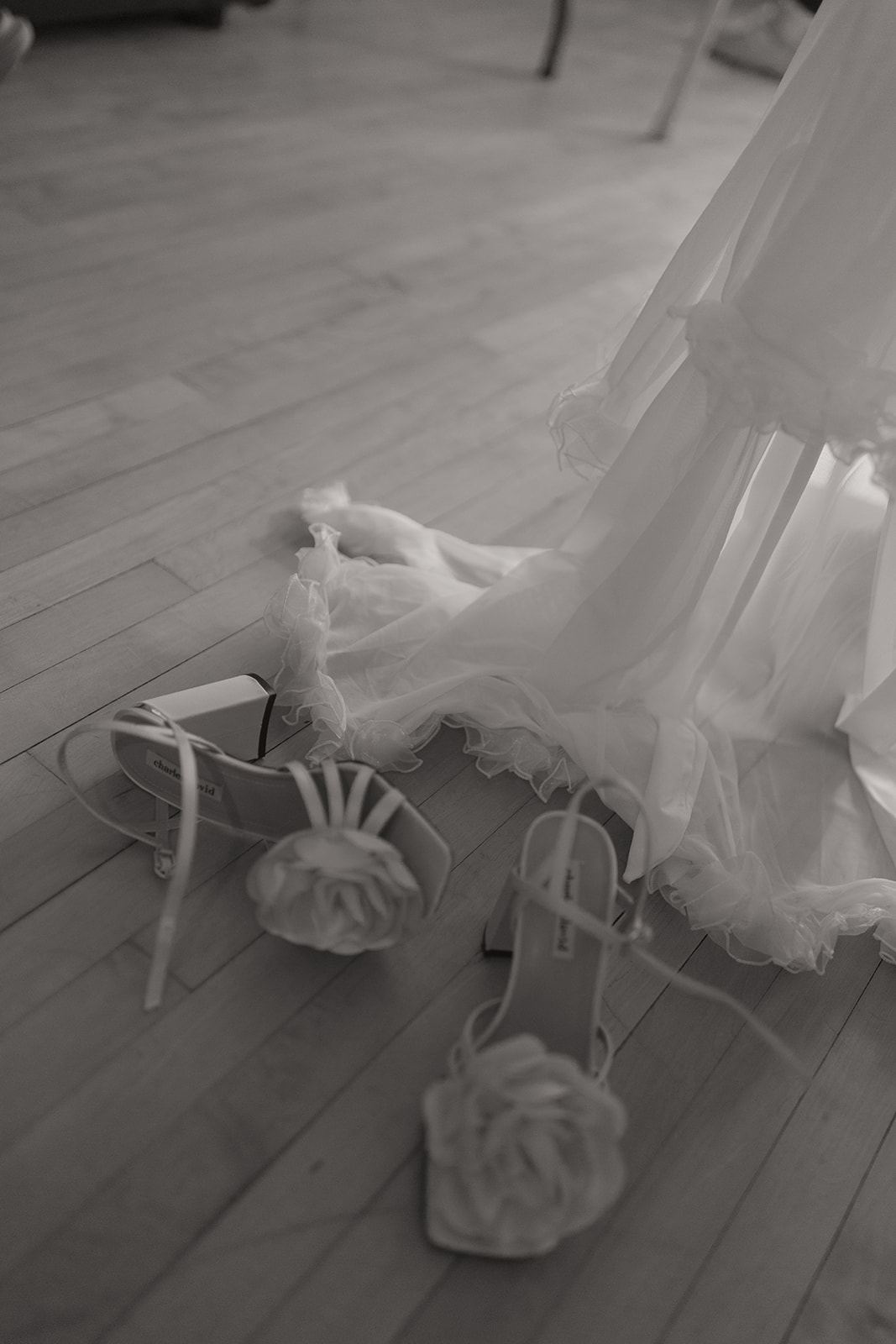 Bridal heels with rosette straps beside a ruffled gown on the floor