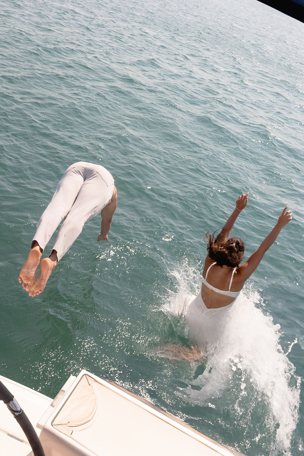Couple diving off a sailboat into the water with a big splash