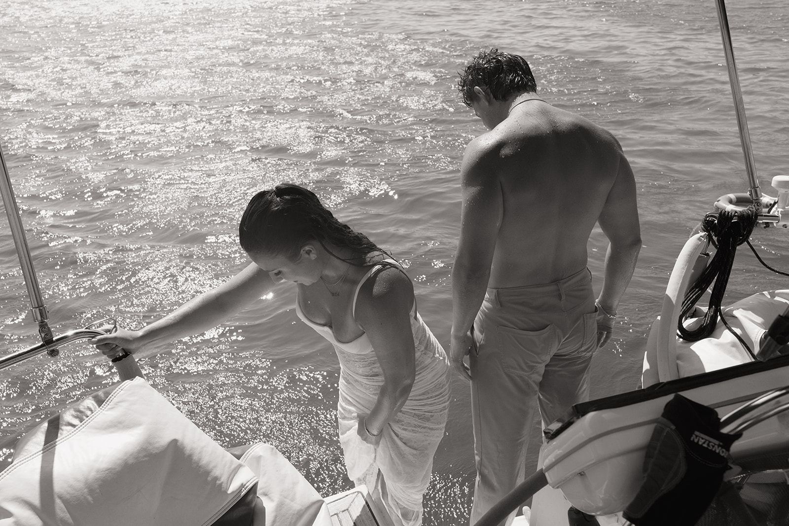Couple climbing back aboard a sailboat on sparkling water, black and white