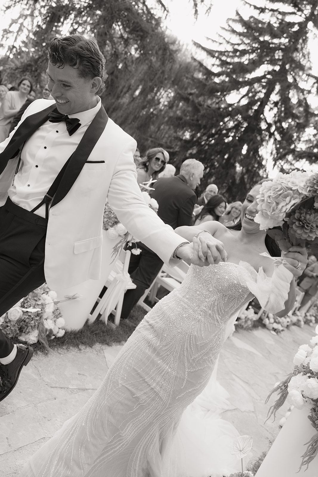Groom in a white tuxedo jacket leading the bride through cheering guests