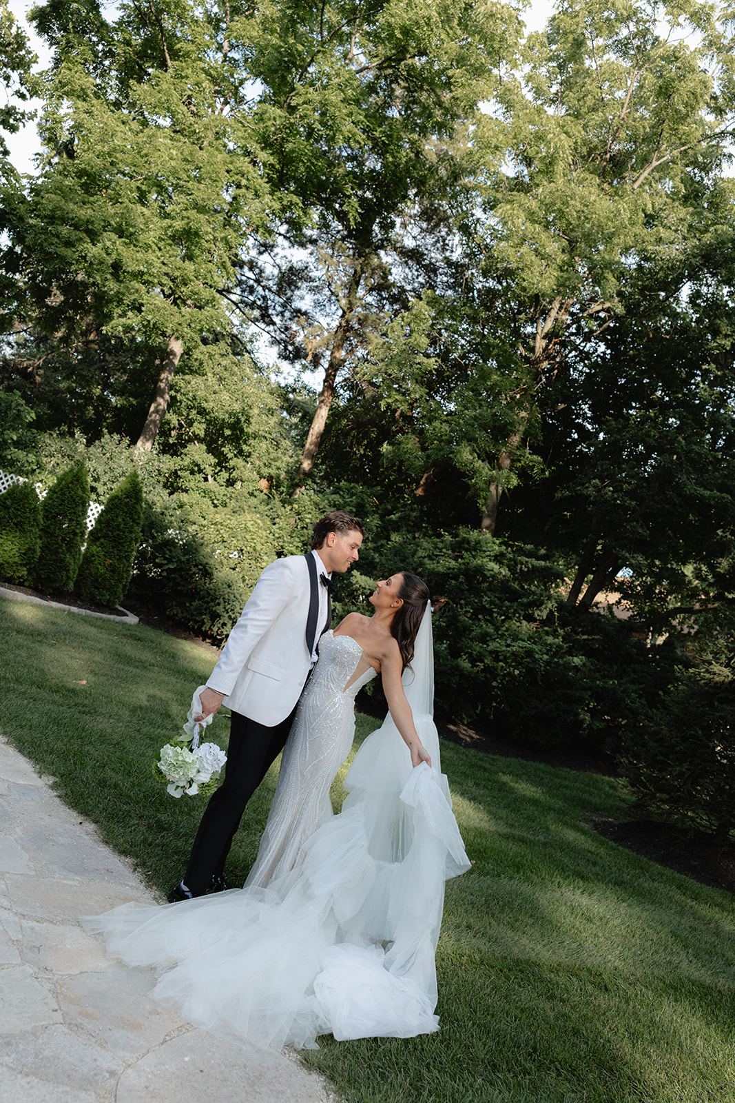 Newlyweds kissing on a garden path surrounded by lush trees