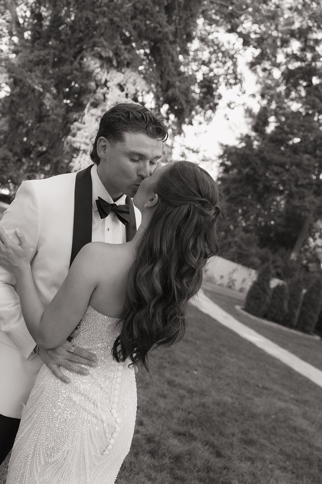 Groom kissing the bride beneath leafy trees