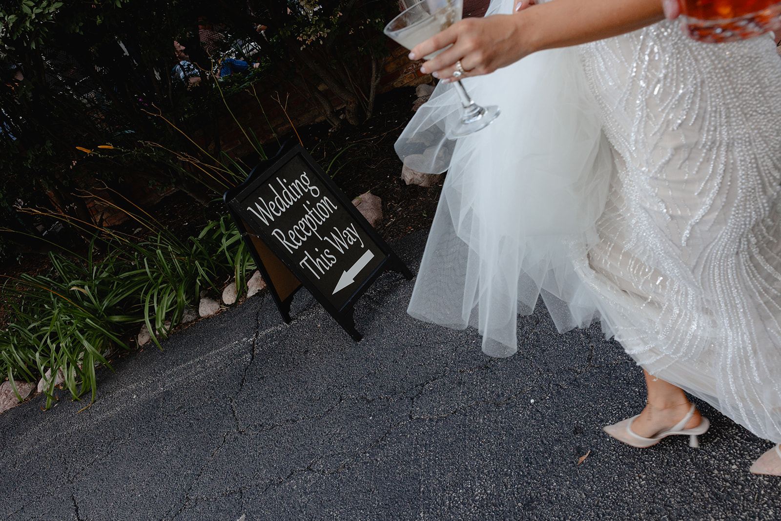 Bride with a drink walking past a 'Wedding Reception This Way' sign