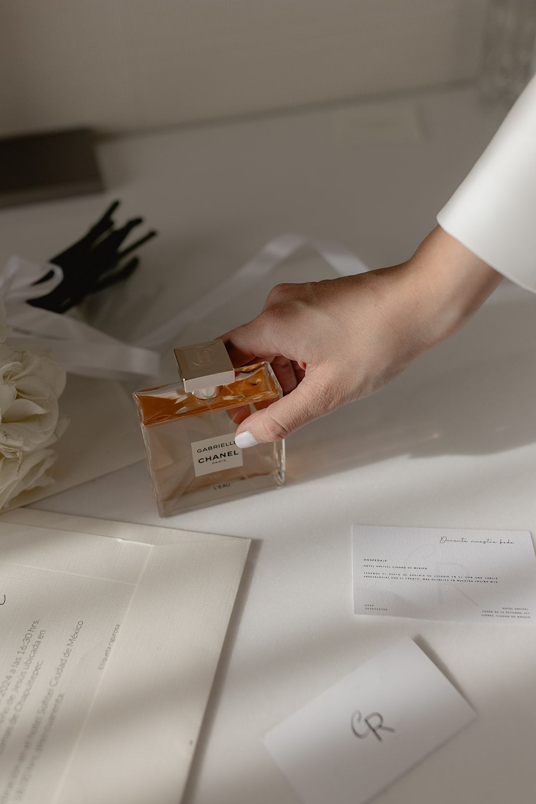 Hand reaching for a Chanel Gabrielle perfume bottle beside wedding stationery