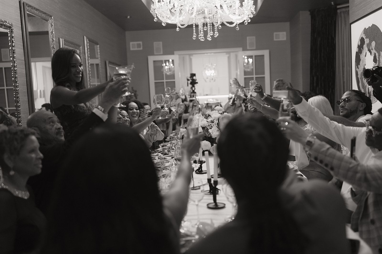 Guests raising their glasses for a toast beneath a crystal chandelier