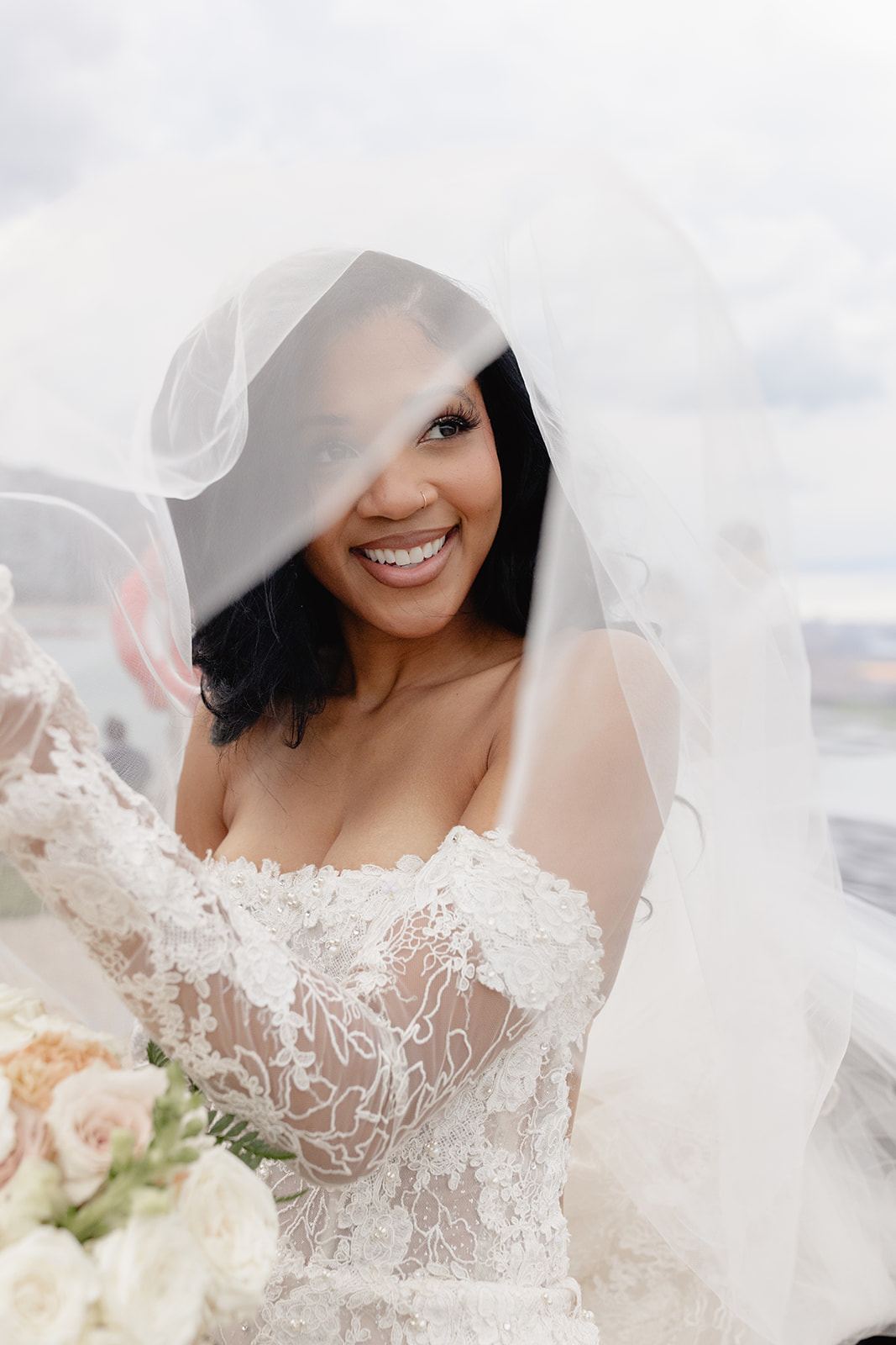 Smiling bride peeking through her veil while holding blush roses