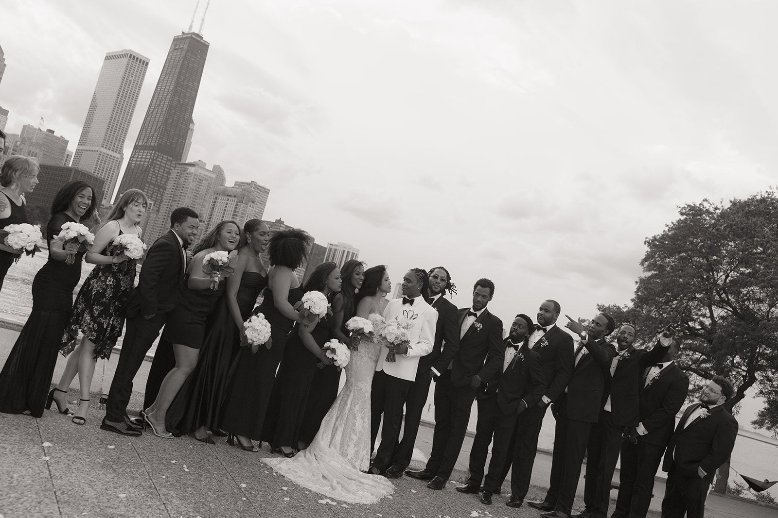 Large wedding party lined up in black attire before the Chicago skyline
