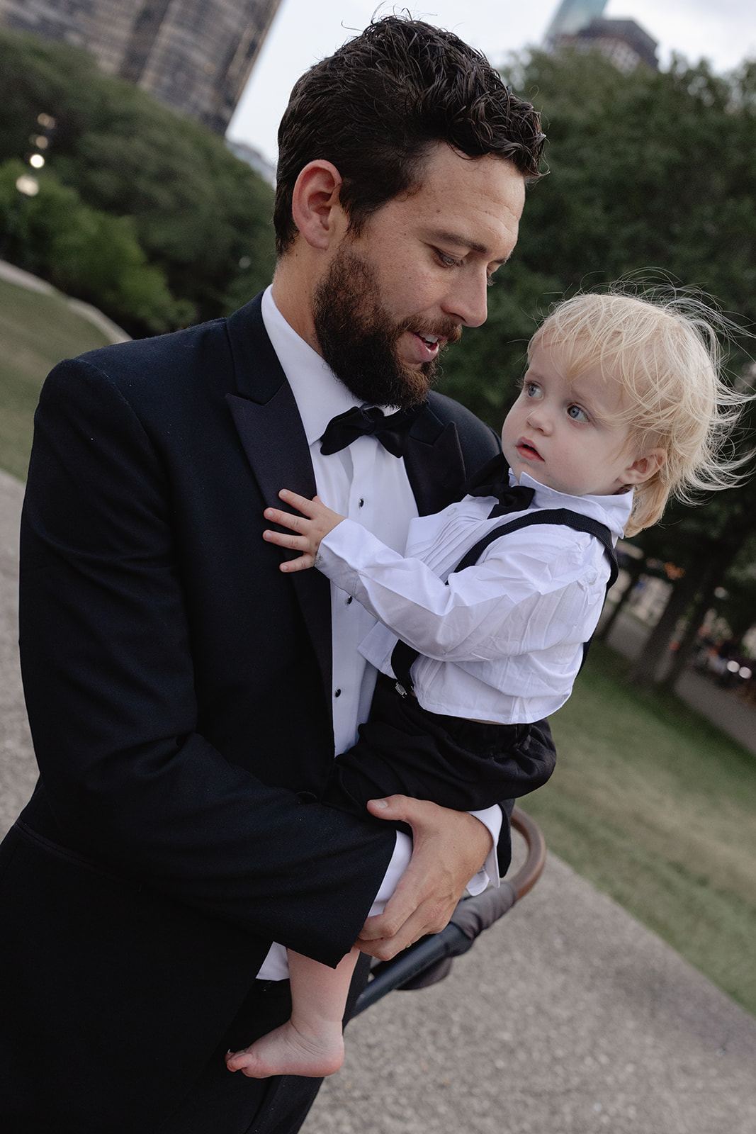 Groom in a tuxedo holding a little blond boy in a matching outfit