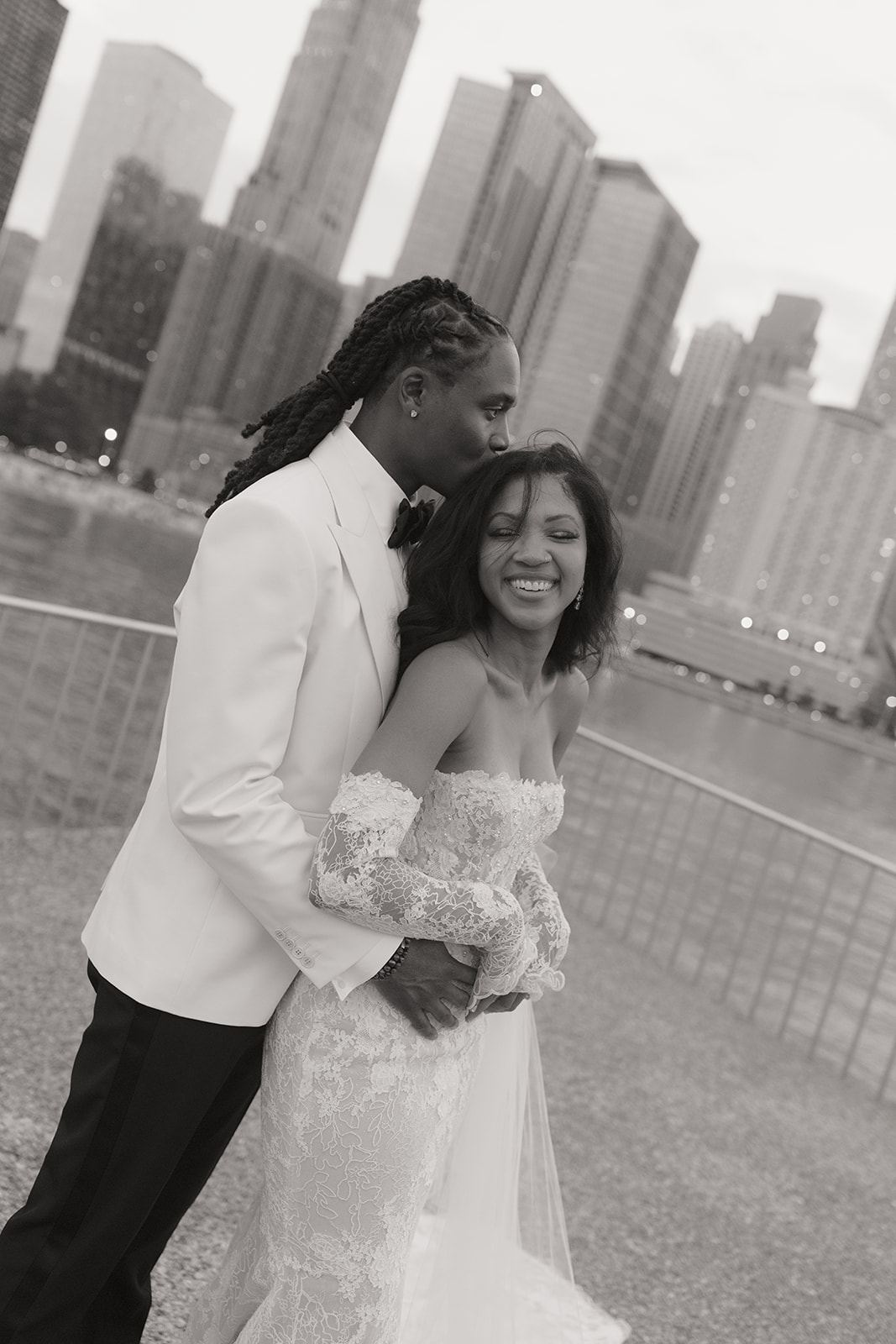 Groom in a white jacket kissing the bride's cheek among city towers