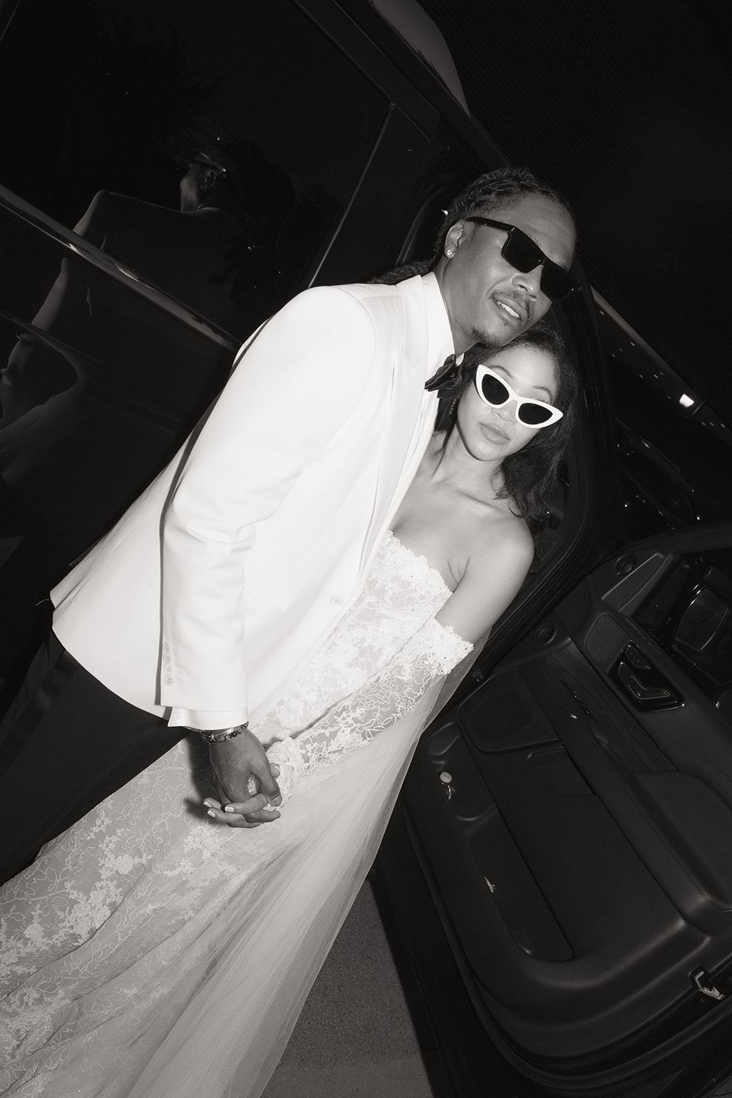 Couple in sunglasses posing by an open car door, black and white