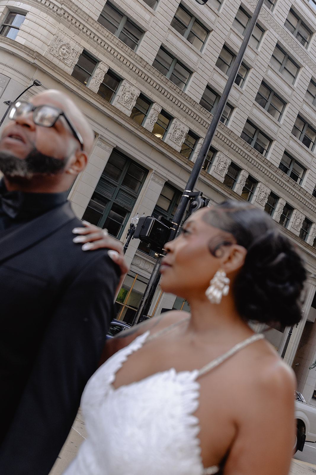 Bride in statement earrings glancing at the groom on a downtown street