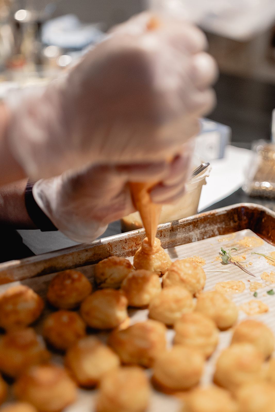 Caterer piping filling into golden pastry puffs on a baking tray