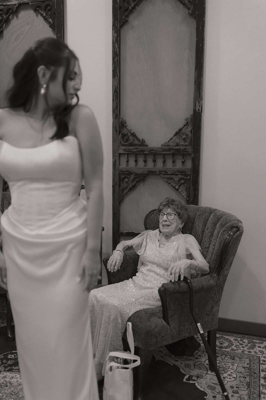 Bride glancing at an elderly woman seated in an ornate armchair