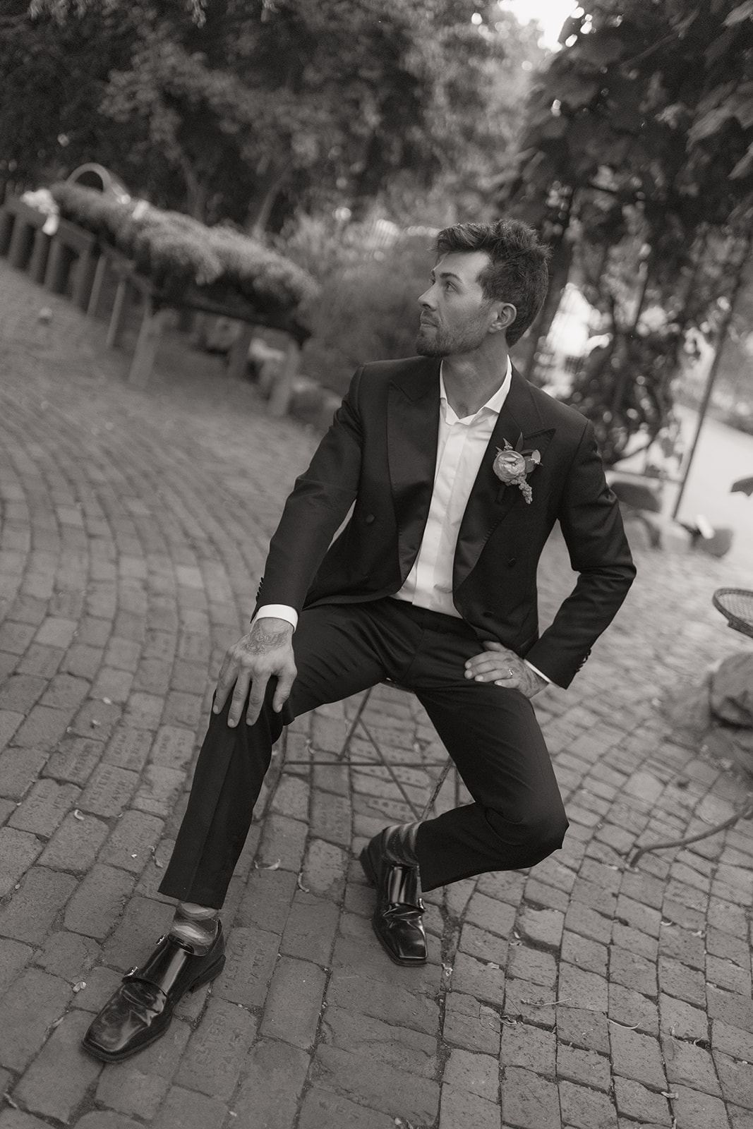 Groom perched on a chair in a cobblestone courtyard, black and white
