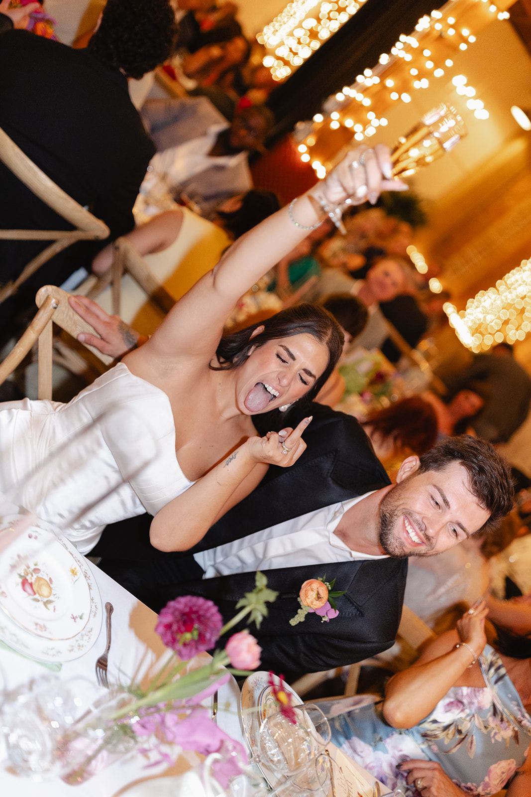 Newlyweds cheering at their reception table under string lights