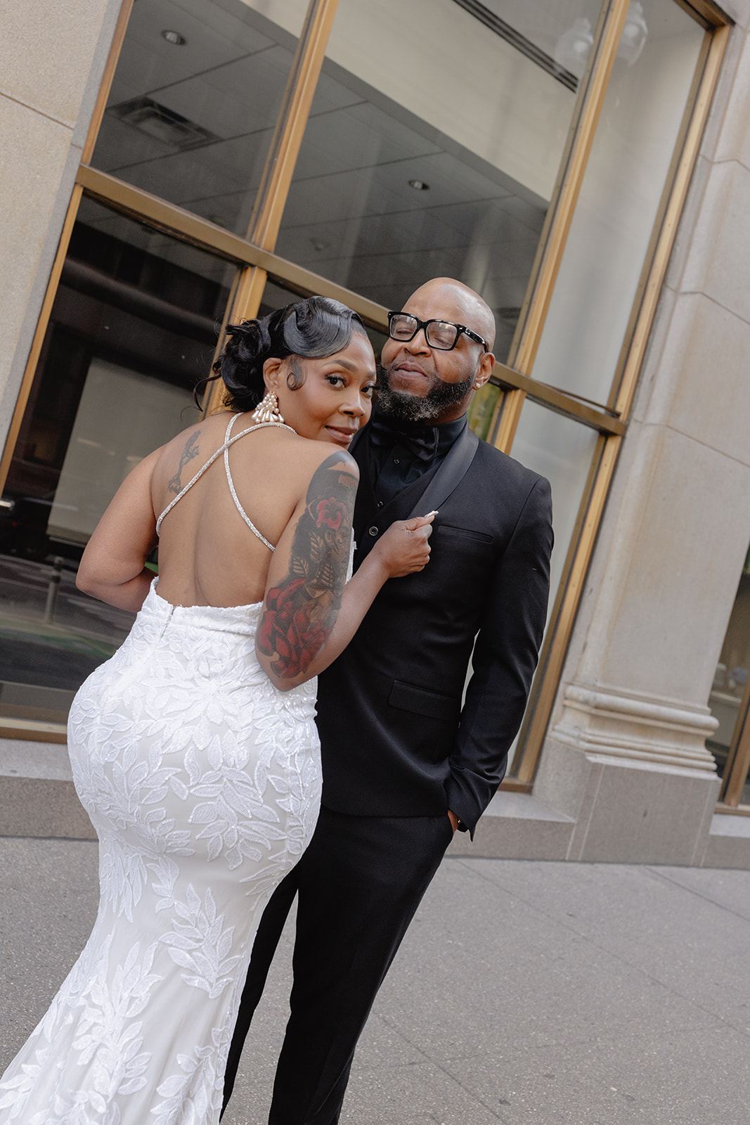 Bride in a backless lace gown posing with the groom on a city sidewalk