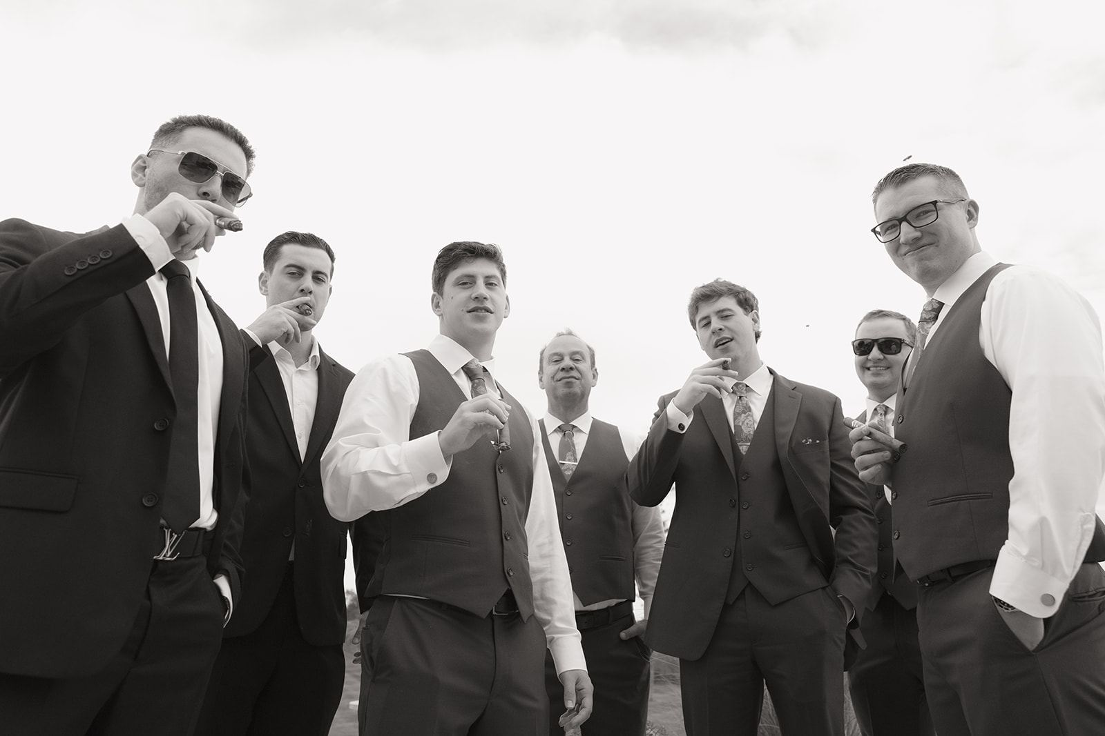 Groomsmen in vests and suits smoking cigars together, black and white