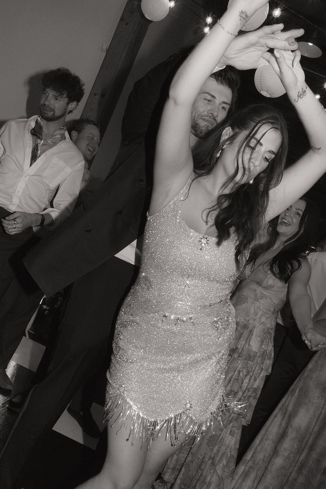 Bride in a sequined minidress dancing with her arms up at the party