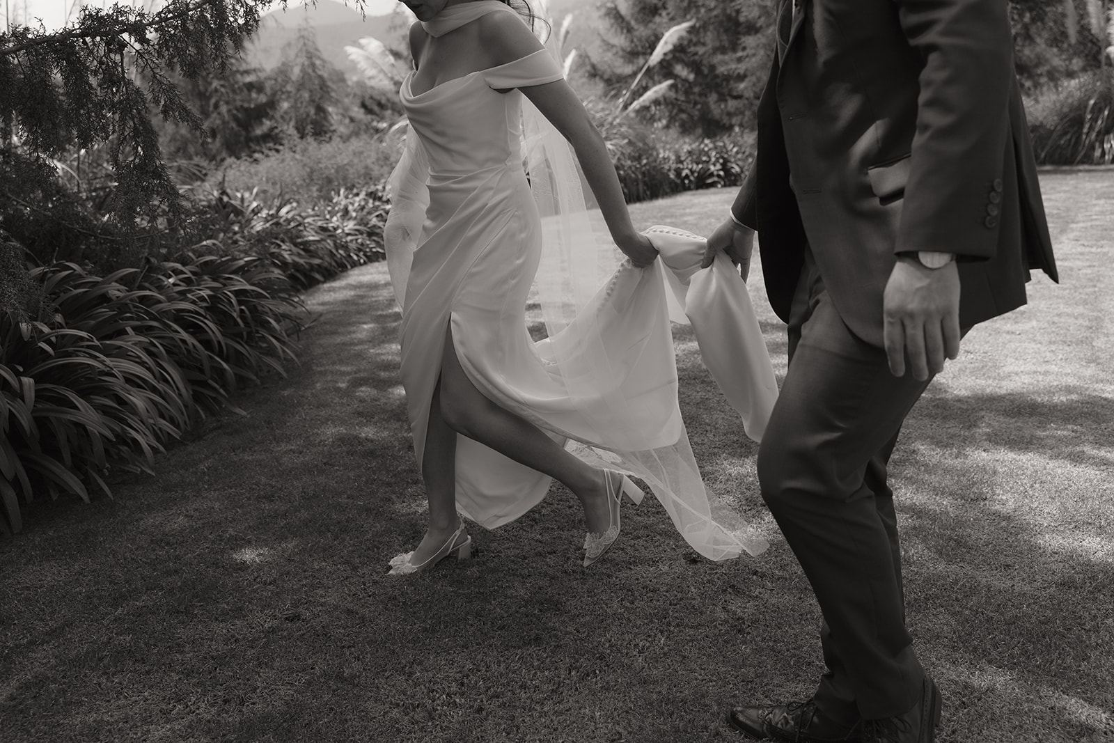 Bride lifting her gown as she walks a garden path with the groom