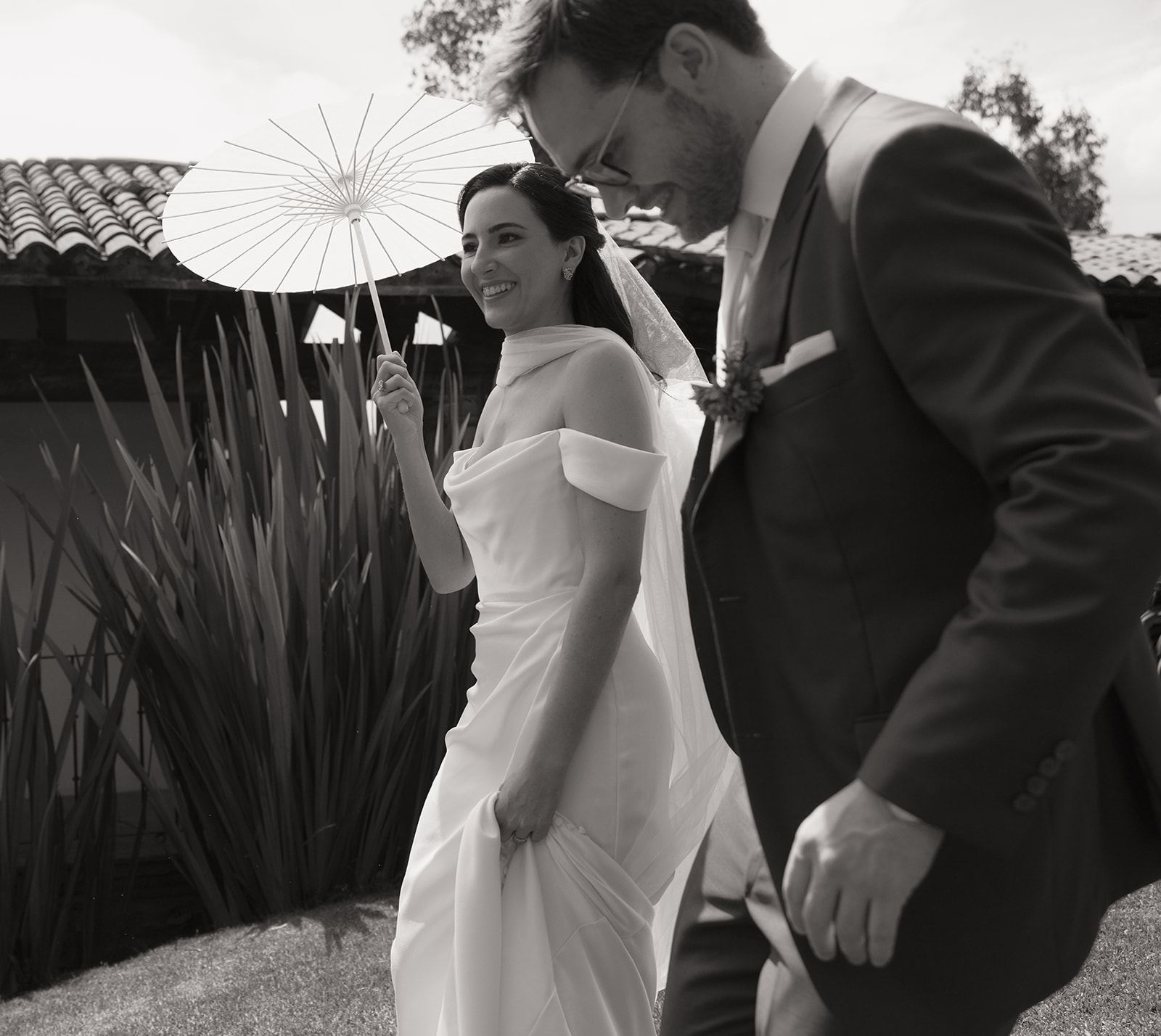 Bride with a paper parasol laughing beside the groom, black and white