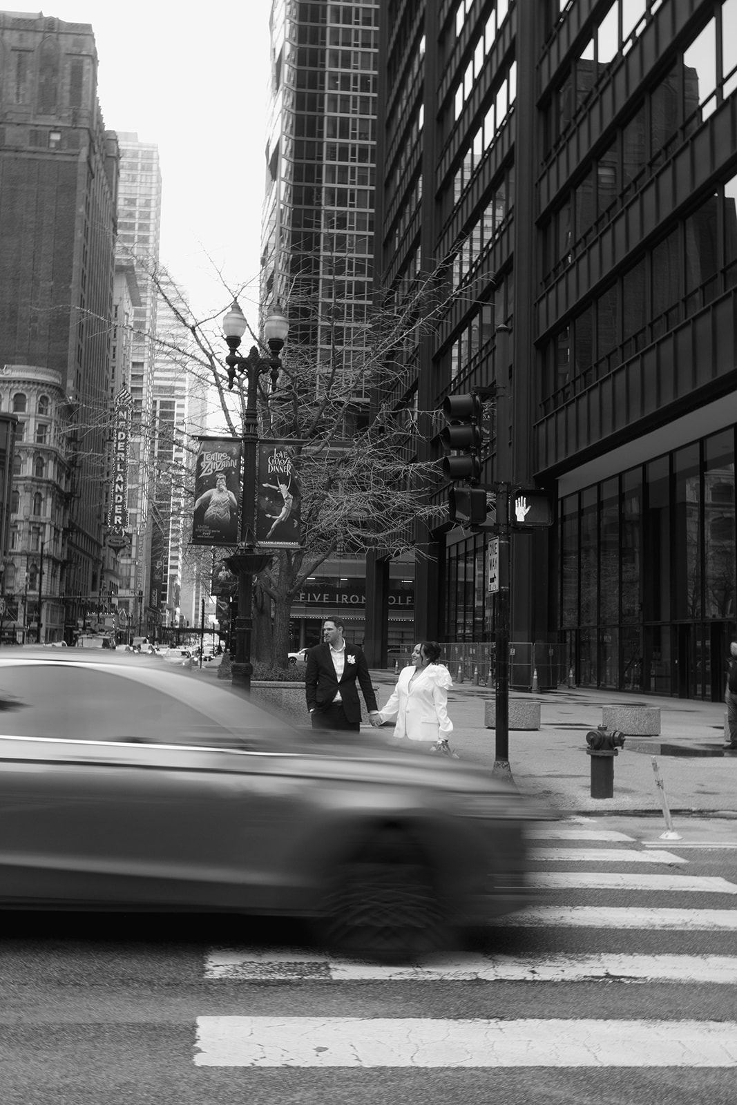 Newlyweds crossing a downtown street as a car speeds past, black and white