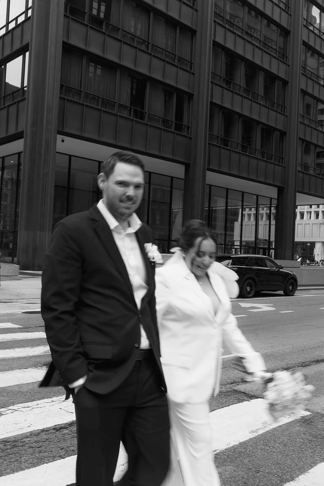 Groom in a dark suit and bride in a white jacket crossing the street