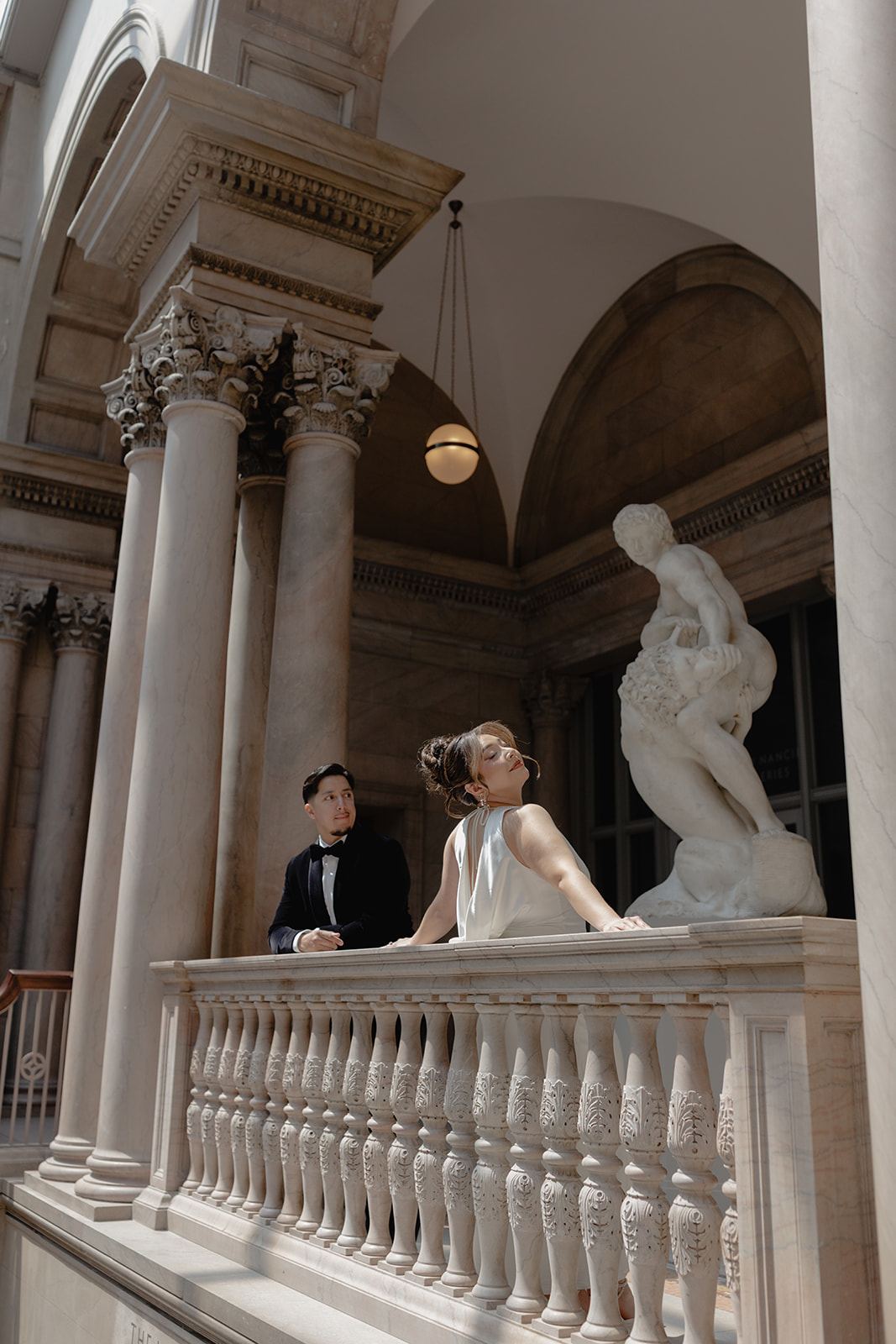 Couple leaning on a marble balustrade beside classical columns and a statue