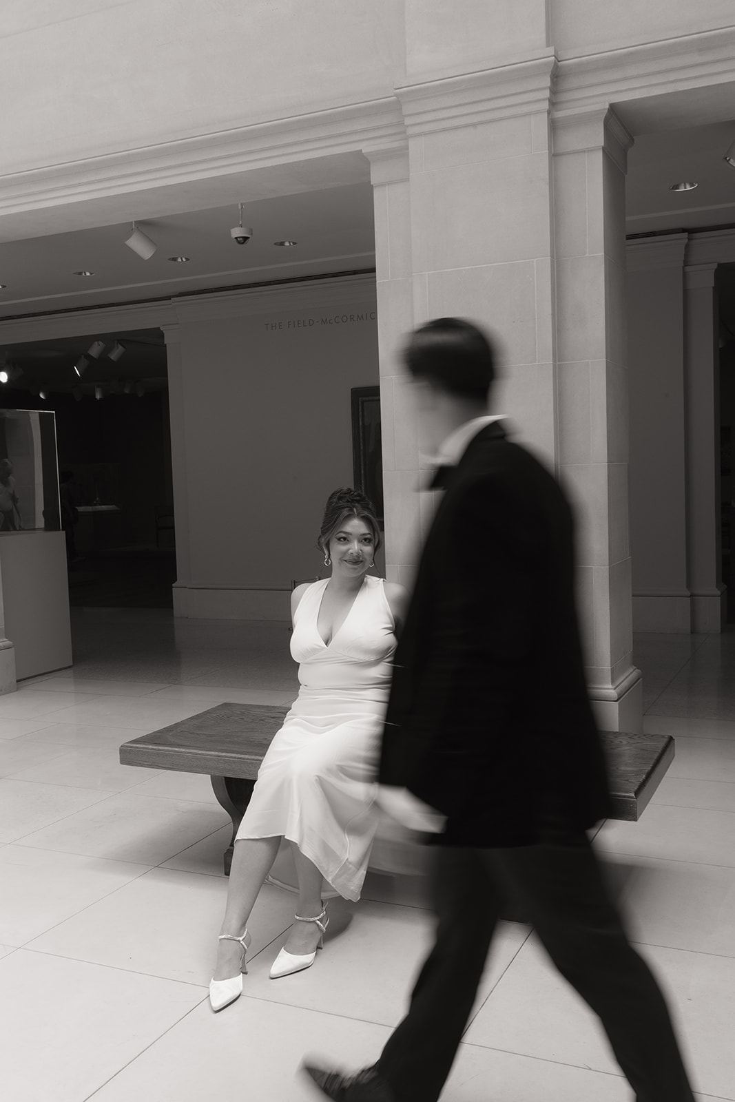 Groom walking past in motion blur as the bride waits on a bench