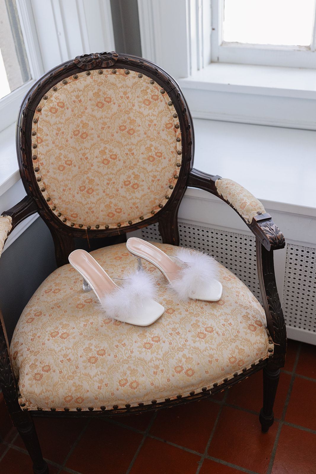 Feather-trimmed bridal heels resting on an antique upholstered chair