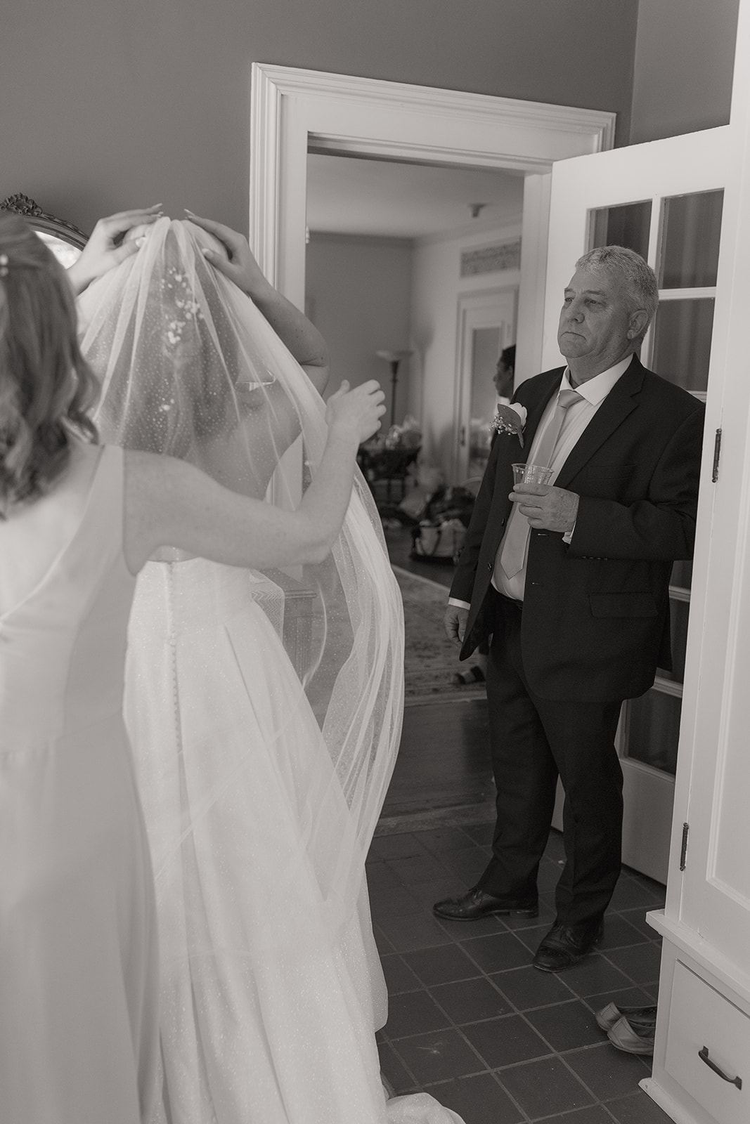Older man in a suit watching the bride as her veil is arranged