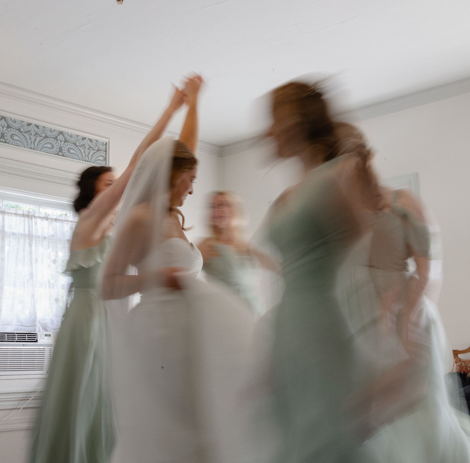 Bride twirling with bridesmaids in sage green dresses, joyfully blurred